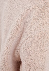 Jasnoróżowa, miękka tkanina o puszystej, miękkiej fakturze z głębokim włosiem. Ogólnie gładka powierzchnia z subtelnymi różnicami w grubości.