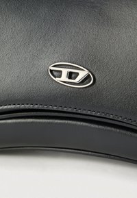 Primo piano di un emblema cromato argentato su una superficie in pelle nera testurizzata con cuciture dettagliate sotto l'emblema.