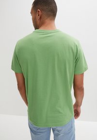 T-shirt in cotone verde con collo a giro e maniche corte. Caratterizzato da una vestibilità comoda e una texture liscia. Nessun motivo o dettaglio visibile.