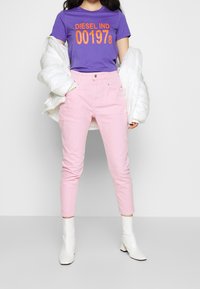 Lila T-shirt med orange text "DIESEL IND. 001978", tillsammans med ljusrosa jeans. En vit pufferjacka bärs över outfiten. Vita klackboots.