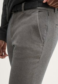 Grijze textuurbroek met een slim fit, voorzien van zijzakken en een zwarte riem. De stof heeft een subtiel visgraatpatroon.