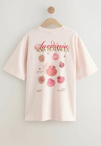 Camiseta de manga corta de color rosa claro con un diseño gráfico de concha y texto "Península de Sinis de Sardeña" en la parte posterior. Material de algodón suave.