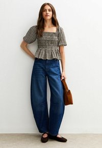 Top ajustado con estampado de cuadros en blanco y negro con mangas abullonadas, combinado con jeans de mezclilla azul de pierna ancha y cintura alta, y bolso marrón de hombro.