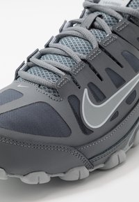 Šedá sportovní bota s prodyšným svrškem, tvarovanými detaily a silnou gumovou podrážkou s polstrovanými body. Logo Nike z reflexního materiálu.