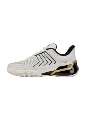 Chaussure de sport basse blanche et noire avec des accents dorés, un motif latéral et une semelle texturée pour une meilleure adhérence, vue de côté.