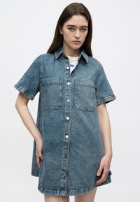 Φόρεμα από τζιν σε ανοιχτό μπλε, με κοντά μανίκια, κλείσιμο με κουμπιά μπροστά, δύο τσέπες στο στήθος και καμπυλωτό τελείωμα, με κουμπιά σε ασημί απόχρωση.