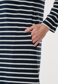 Marinblå och vit randig långärmad klänning med ficka, tillverkad av ett mjukt material och med en avslappnad passform. Fickan är subtilt integrerad i designen.