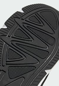 Svart sneaker-sula med en texturerad gummiyta och triangulära mönster samt räfflor för grepp. Vita accenter nära kanten.