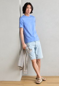 Lyseblå bomull T-skjorte, denimshorts, holder en rutete skjorte. Uformelle sandaler. Enkelt design, avslappet passform og myk tekstur.