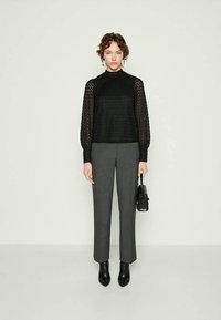 Blusa de renda preta com mangas longas e balonê. Calças cinzas sob medida, ajustadas na cintura, e botins pretos. Bolsa minimalista preta.