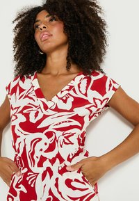 Vestido con estampado floral en rojo y blanco, de mangas cortas, escote en V profundo y bolsillos. La tela parece ligera y transpirable.