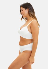 Ensemble de lingerie blanche comprenant un bralette doux avec des bordures en dentelle et une culotte assortie. Tissu lisse avec des accents en dentelle délicate. Vue de profil.