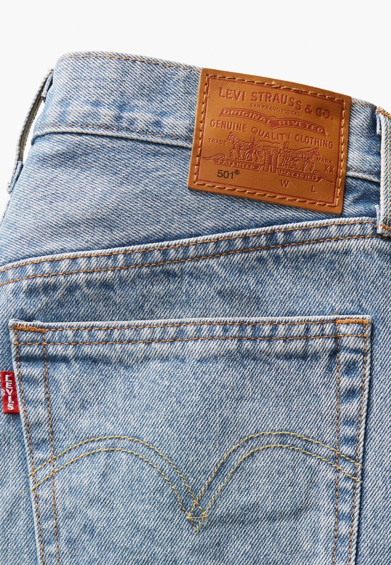 Jeans in denim blu con un'etichetta in pelle, cuciture arancioni a contrasto e un design distintivo della tasca posteriore con un'etichetta rossa.