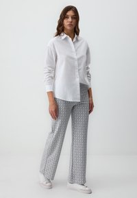 Chemise blanche à bouton avec des manches longues ; pantalon gris clair à motifs avec un subtil design géométrique ; baskets blanches.