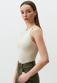 Beige geripptes Tanktop mit schmalen Trägern, strukturiertem Stoff und tailliertem Design, kombiniert mit hochgeschnittenen olivgrünen Hosen.