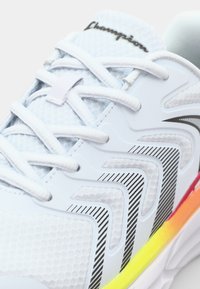 White athletic shoe with a textured mesh upper, striped detailing in black, and a multicolored sole gradient from pink to yellow.