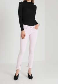 Top negro de manga larga con escote en forma de ondas, combinado con pantalones skinny rosa claro con cremalleras en el dobladillo, luciendo tacones altos negros.