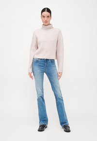 Pull à col roulé en rib à rayures rose clair associé à un jean évasé bleu. Tissu texturé, coupe décontractée et chaussures noires avec des clous.