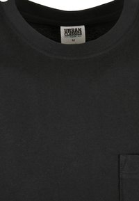 T-shirt noir en coton avec col rond, étiquette visible taille medium et une petite poche sur le côté droit.