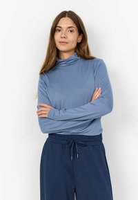 Ljusblå långärmad polotröja i mjukt material, kombinerad med mörkblå elastiska midjebyxor i sweatmaterial med en avslappnad passform.