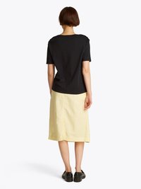Black short-sleeve top with a round neckline, paired with a knee-length yellow skirt and black platform shoes. Smooth fabric texture.
