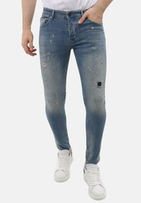 Vervaagde blauwe denim jeans met versleten accenten en meerdere scheuren. Slanke pasvorm, vijf-pocket ontwerp, gecombineerd met witte sneakers.