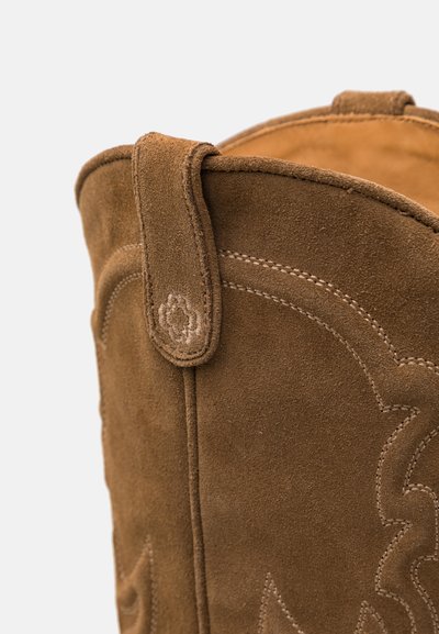 Brūni zamšaini rietumu zābaki ar dekoratīvu izšuvumu, noapaļotu augšu un nelielu cilpiņu pie apkakles, kas nodrošina ērtu uzvilkšanu.