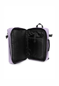 Mochila lila con apertura con cremallera, que presenta un interior negro, un bolsillo organizador y asas resistentes a los lados.