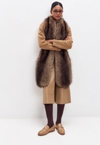 Hnědý svetr s umělou kožešinou, sukně po kolena béžové barvy, hnědé punčochy a béžové mokasíny se zlatými detaily.
