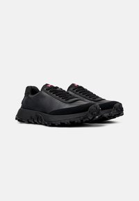 Black sneakers featuring a textured leather upper, suede accents, and a rugged tread outsole. Laces and branding in contrasting red.