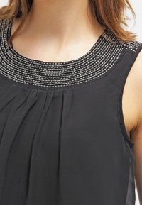 Top senza maniche nero con un design a pieghe e una scollatura decorativa impreziosita da perline con accenti argentati. Tessuto liscio con una consistenza morbida.