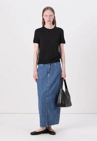 Svart t-shirt, jeans-maxikjol i blått och svarta platta skor. Åtföljd av en handväska i svart läder. Enkel, avslappnad outfit mot en neutral bakgrund.