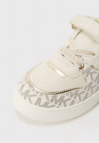 Zapatilla blanca con acentos dorados, superficie texturizada con perforaciones y un patrón impreso. Sujeta con una cinta de Velcro y cordones.