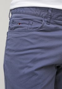 Ljusblå bomullspyjamas med en mjuk textur, med en liten röd, vit och blå logotyp på framfickan och standardfickstickning.