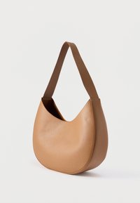 Τσάντα ώμου σε σχήμα ημισελήνου από δέρμα ταμπά με φαρδιά λουρί ώμου, μινιμαλιστικό σχέδιο και υφή επιφάνειας σε απλό φόντο.
