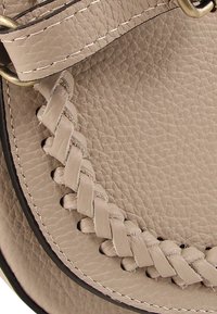 Beige leren handtas met gevlochten details langs de rand, voorzien van zichtbare stiksels, een gladde textuur en een ronde vorm.