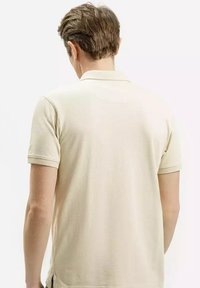 Beżowa bawełniana koszulka polo z klasycznym kołnierzykiem, krótkimi rękawami i subtelną teksturą. Posiada boczne rozcięcia u dołu, co zapewnia swobodę ruchów.