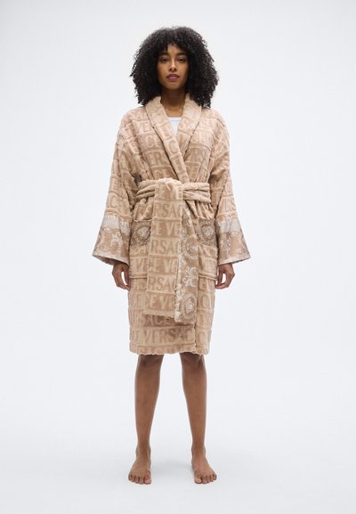 Μπεζ μπουρνούζι από πετσετέ ύφασμα με μοτίβο λογότυπου "VERSACE", ζώνη και λεπτομερές περίγραμμα. Διαθέτει μακριά μανίκια και άνετη εφαρμογή.