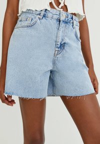 Shorts en denim bleu clair avec une taille haute, un ourlet effiloché et un design classique à cinq poches. Couture reconnaissable près des poches et des boutons.