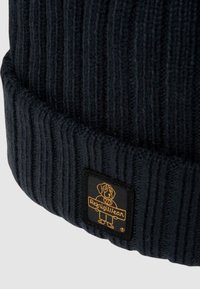 Berretto a coste di colore blu scuro con risvolto. Presenta una toppa quadrata nera con un logo giallo di un cane e il nome del marchio, RefrigiWear.
