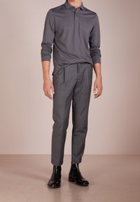 Szara polo koszula z długim rękawem i kołnierzykiem na trzy guziki; połączona z dopasowanymi szarymi spodniami i czarnymi botkami sięgającymi kostki, o gładkiej fakturze.