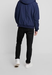 Marineblaue Kapuzenjacke mit lässigem Design, kombiniert mit schwarzen Slim-Fit-Jeans und weißen Sneakers. Glatte Textur, schlichte Akzente.
