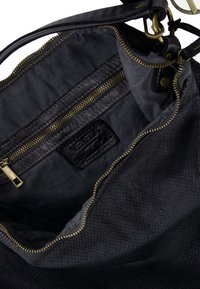 Indvendig i en sort tekstureret lædertaske med en lynlåslomme, gylden lynlås og et synligt mærke. Foringen er mørkegrå stof.