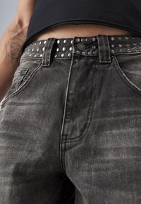 Svarta denimjeans med en urtvättad textur, med ett nitar svart bälte, robust metallbeslag och standard fickplaceringar.