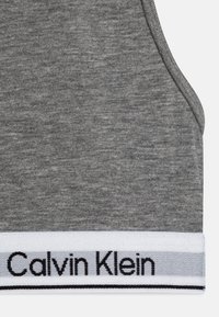 Sivi pamučni top bez rukava s rebrastom teksturom i kontrastnim bijelim pojasom s natpisom "Calvin Klein" u crnim slovima duž donjeg ruba.