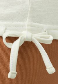 Un tessuto beige chiaro con una consistenza morbida presenta una sezione marrone a contrasto. Un nastro bianco legato in vita aggiunge dettaglio e funzionalità.
