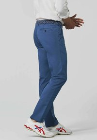 Blauwe chinos van katoen, met een rechte snit. Een gestreepte riem wordt op de taille gedragen; witte sneakers met rode en blauwe accenten maken de look compleet.