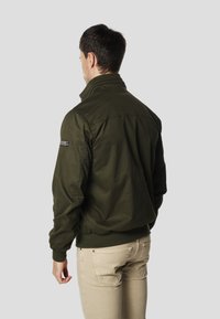 Bomberka w kolorze oliwkowej zieleni z prążkowanym dołem i mankietami, wyposażona w stójkę i teksturowaną powierzchnię. Widok od tyłu ukazuje detal z logo.