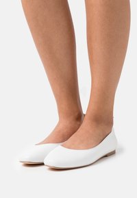 White leather ballet flats with a rounded toe, minimalistic design, and a flat sole. Smooth texture with a simple, sleek silhouette.