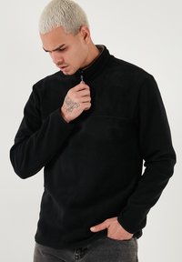 Pullover in pile nero con colletto alto, chiusura a zip a metà, e maniche lunghe. Tessuto liscio con dettagli di cucitura minimi.